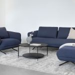 Photo présentant un salon avec un canapé 3 places, un fauteuil et un pouf. Il y a deux finitions tissu bleu marine et pied en métal noir matte.